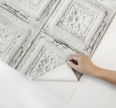 a person is painting on the wall with white paint and some decorative tiles behind them