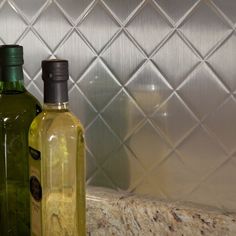 two olive oil bottles sitting on top of a counter next to a tile backsplash