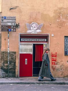 a woman walking down the street in front of a building with a red door and sign on it