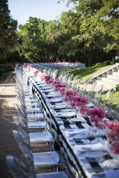 a long table is set with clear chairs and pink flowers