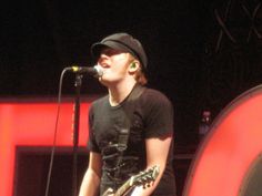 a man with a guitar standing in front of a microphone and wearing a black t - shirt