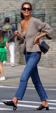 a woman walking across the street in jeans and heels with her hand on her hip