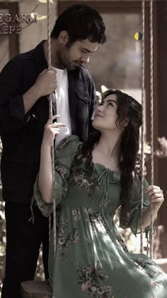 a woman sitting on a swing with a man standing next to her and looking at her