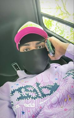 a person wearing a pink hat and holding a cell phone up to their face while sitting in a car