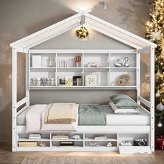 a white bed sitting under a christmas tree next to a shelf filled with books and toys