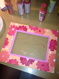 there is a pink and orange flowered frame on the table with other crafting supplies around it