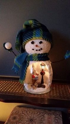 a snowman in a hat and scarf is inside a glass jar with lights on it