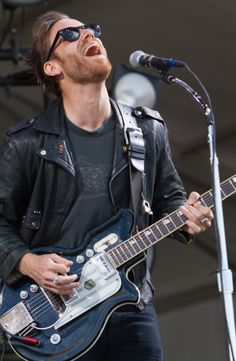 a man singing into a microphone and playing an electric guitar at a music festival with his eyes closed