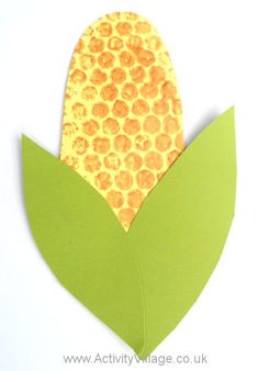 an origami corn on the cob is cut out from green paper and sits on a white surface