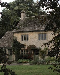 an old stone house with ivy growing on it's roof and windows, surrounded by greenery