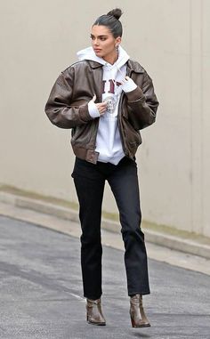 a woman walking down the street wearing black pants and a brown jacket with white hoodie