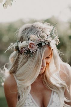 a woman with long blonde hair wearing a flower crown and holding her hand on her shoulder