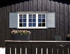 a black wooden building with two windows and flowers in the window box on the bench