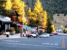 cars are parked on the street in front of buildings and trees with yellow leaves around them