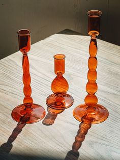 three orange glass candlesticks sitting on top of a wooden table