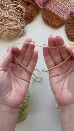 two hands holding yarn and crochet hooks next to balls of yarn on a table