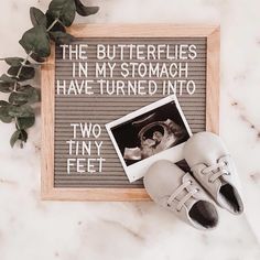 a pair of shoes sitting on top of a table next to a framed photo with the words, the butterflies in my stomach have turned into two tiny feet