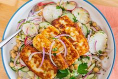 a white bowl filled with fish, cucumber and radishes on top of a wooden table