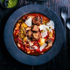 a bowl filled with meat and vegetables on top of a table next to silverware