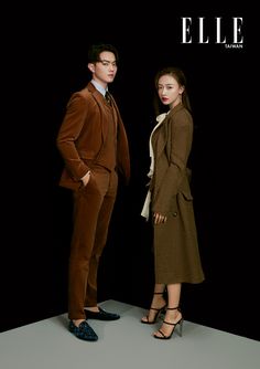 two people standing next to each other in front of a black background wearing brown suits