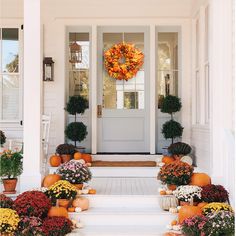 a front porch with potted plants and pumpkins on the steps, next to a white door