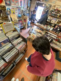 a woman standing in front of a store filled with records and cds on the floor