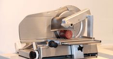 a meat slicer sitting on top of a white counter next to a red object