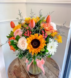 a vase filled with sunflowers and other flowers on top of a wooden table