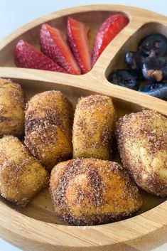 a wooden bowl filled with doughnuts and strawberries next to other food items