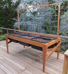 a wooden bench with plants in it on a deck near some trees and bushes,