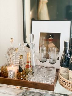 bottles and glasses are sitting on a tray next to a framed photograph with a woman in the background