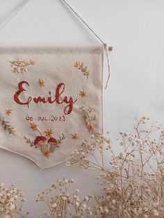 an embroidered banner hanging on a wall next to some dried flowers and branches with the word family printed on it