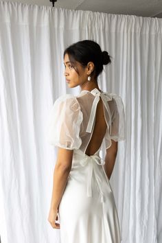 the back of a woman wearing a white dress with sheer sleeves and an open neckline