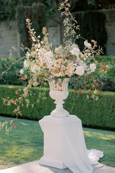 a white vase filled with lots of flowers on top of a lush green park area