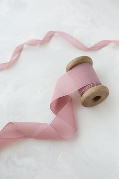 a spool of pink satin ribbon with wooden spools on white fabric background