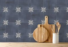 two wooden utensils and a cutting board sit on a table in front of a blue tiled wall