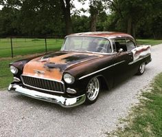 an old car is parked on the side of the road in front of some trees