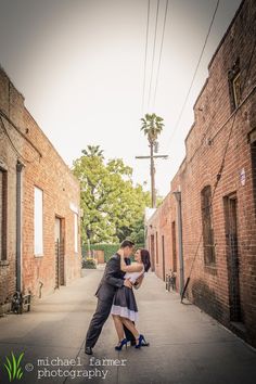 a man and woman kissing in an alleyway between two brick buildings on a sunny day