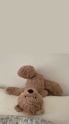 a teddy bear laying on top of a bed next to another stuffed animal in the corner