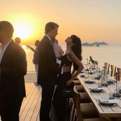 a group of people standing on top of a wooden deck next to the ocean at sunset