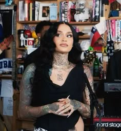 a woman with tattoos holding a microphone in front of a book shelf filled with books