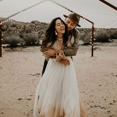 a man and woman hugging each other in the middle of a desert with lights strung overhead