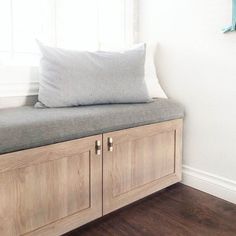 a wooden bench with a cushion on top of it in front of a white wall