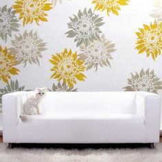 a white dog sitting on top of a couch in front of a floral wallpaper