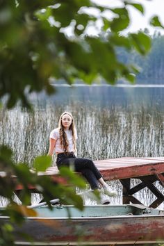 a young woman sitting on top of a wooden bench next to a body of water