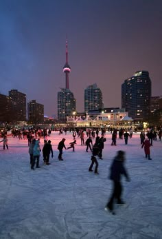 many people are skating on an ice rink in front of the city skyline at night