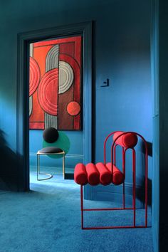 a room with blue walls and red chairs in the foreground, an abstract painting on the wall