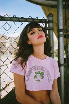 a woman in a pink shirt leaning against a fence with her hands on her hips