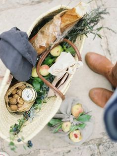 a person is holding a basket full of food and other items on the ground next to them