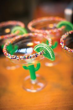 three margarita glasses with sprinkles and lime slices in them on a table